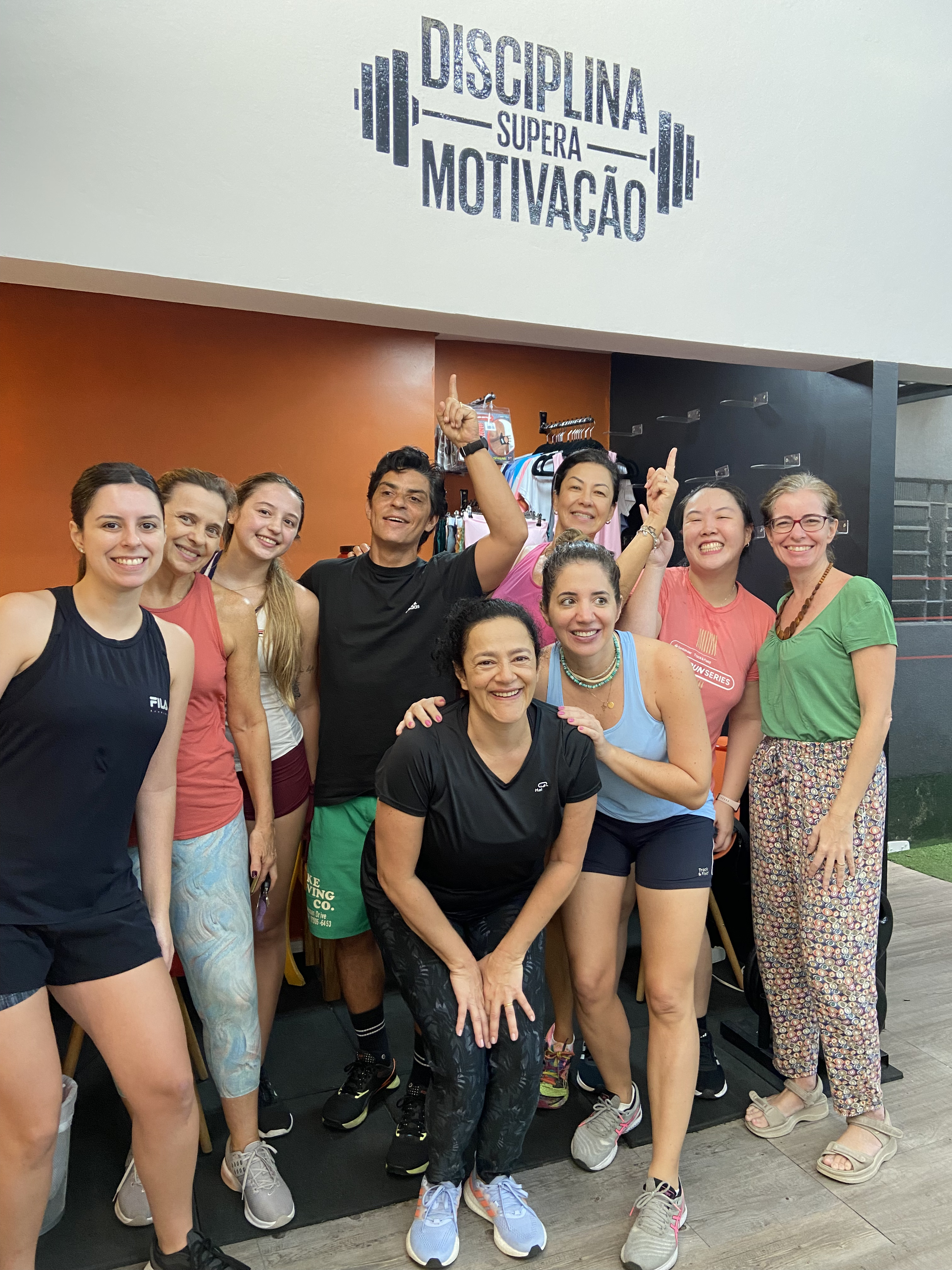 Grupo de alunas e alunos do Team Capita sorrindo ao lado de Dalton sob o letreiro Disciplina supera motivação